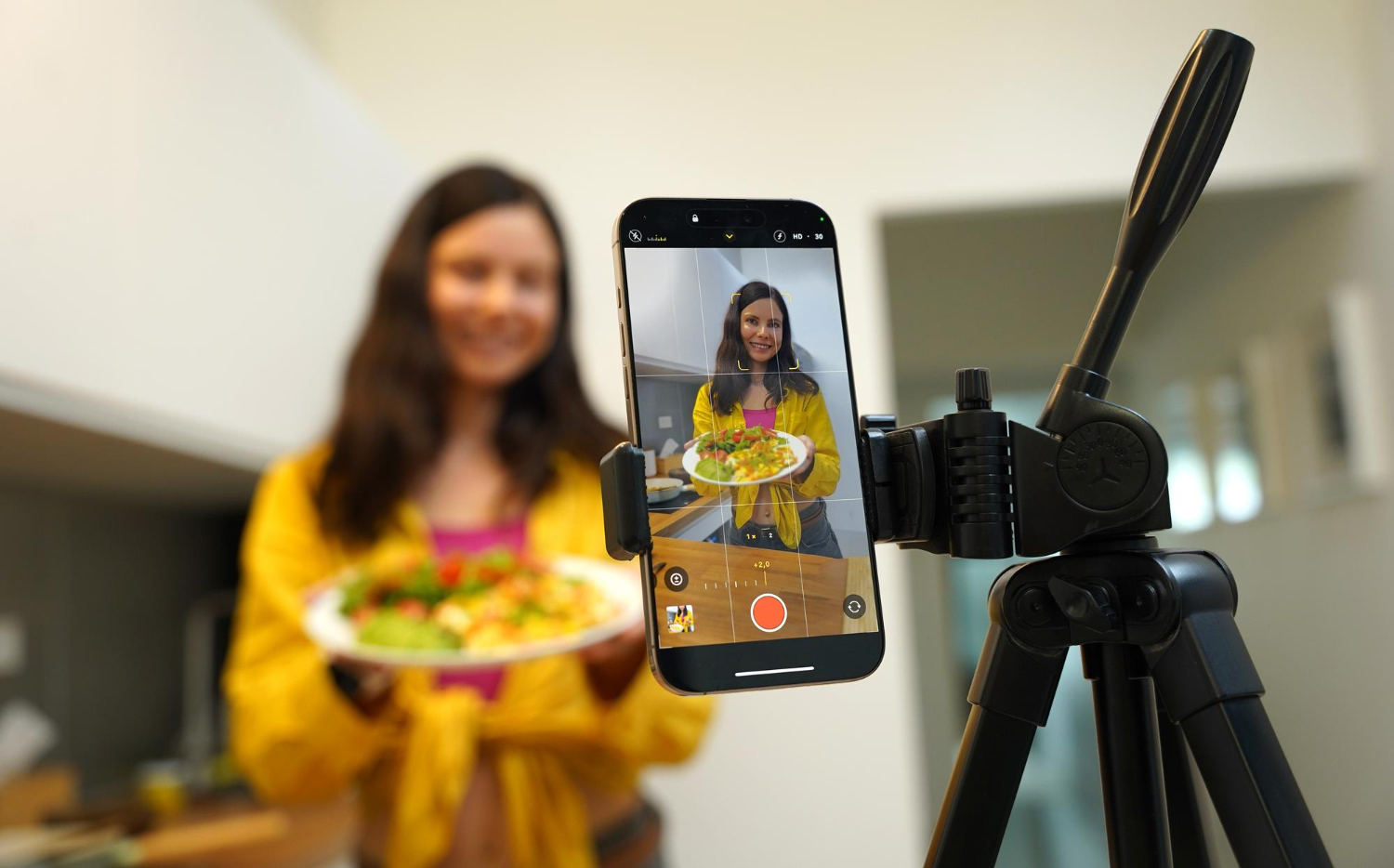mulher aparecendo na tela de um celular segurando um prato de comida representando a criação de conteúdo para as redes sociais