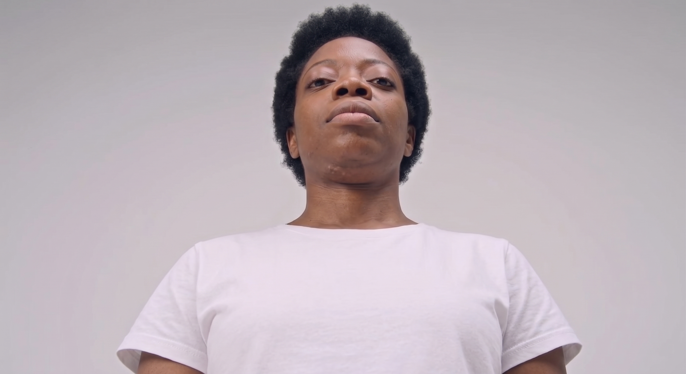 Tipos de ângulo: contra-plongée. Uma mulher ao centro da imagem, usando calça jeans e camiseta branca, enquadrada com a câmera de baixo para cima