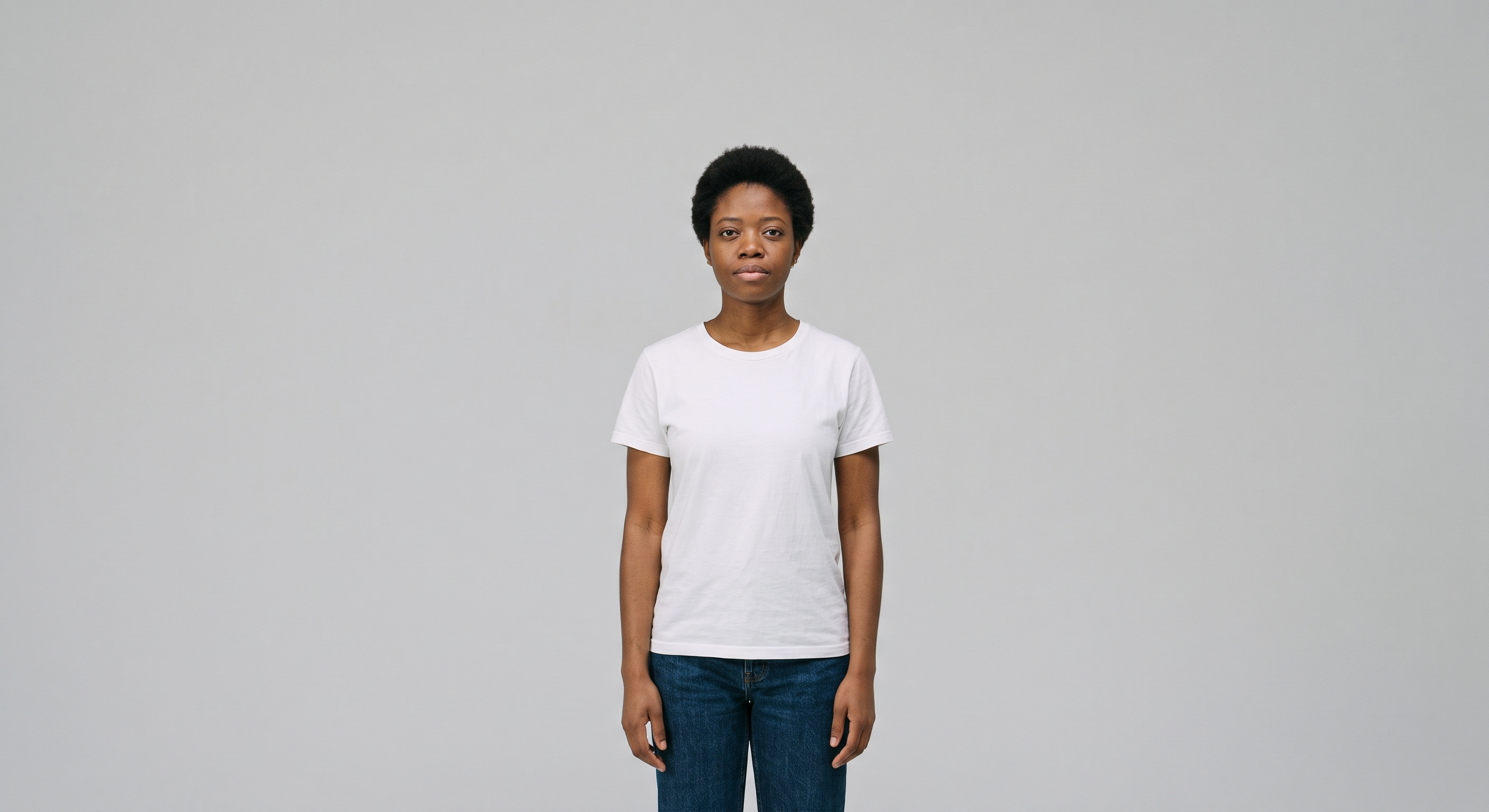 Tipos de plano: plano americano. Uma mulher ao centro da imagem, usando calça jeans e camiseta branca em plano americano, dos joelhos para cima, com um fundo neutro.