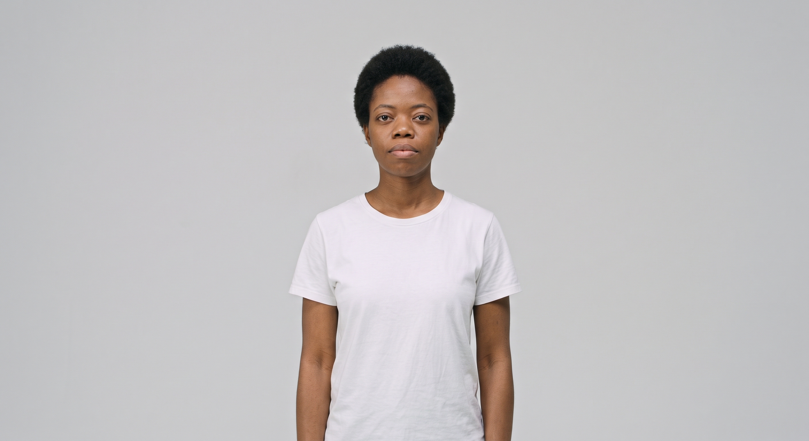 Tipos de plano: plano médio. Uma mulher ao centro da imagem, usando calça jeans e camiseta branca em plano médio, da cintura para cima, com um fundo neutro.