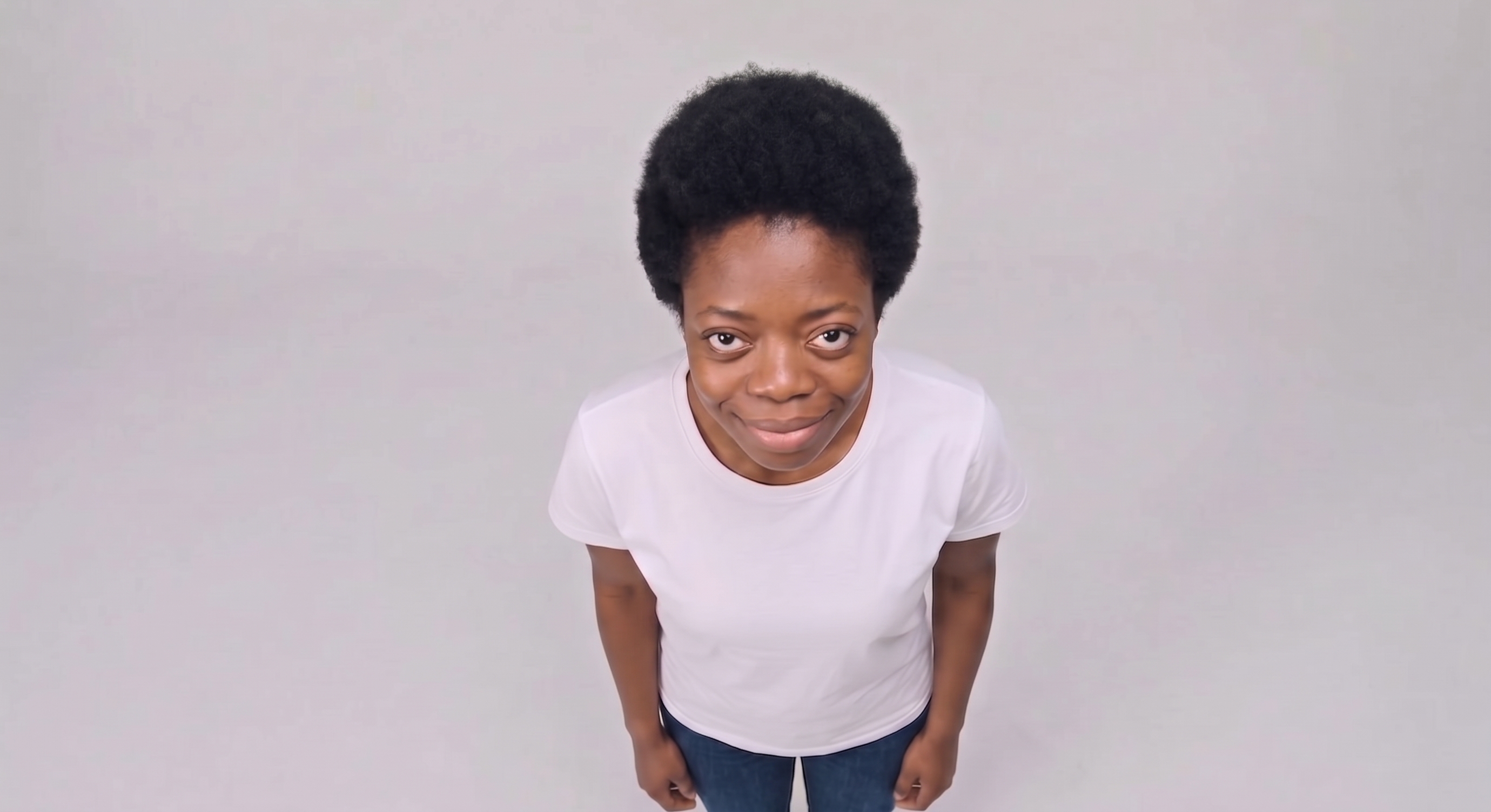 Tipos de ângulo: plongée. Uma mulher ao centro da imagem, usando calça jeans e camiseta branca, enquadrada com a câmera de cima para baixo.